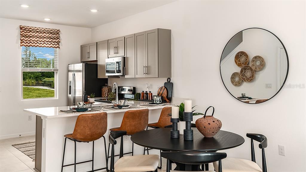 A kitchen with gray cabinets, stainless steel appliances, and a dining area with a mirror — 10600 ORBIT TERRACE, SARASOTA, FL