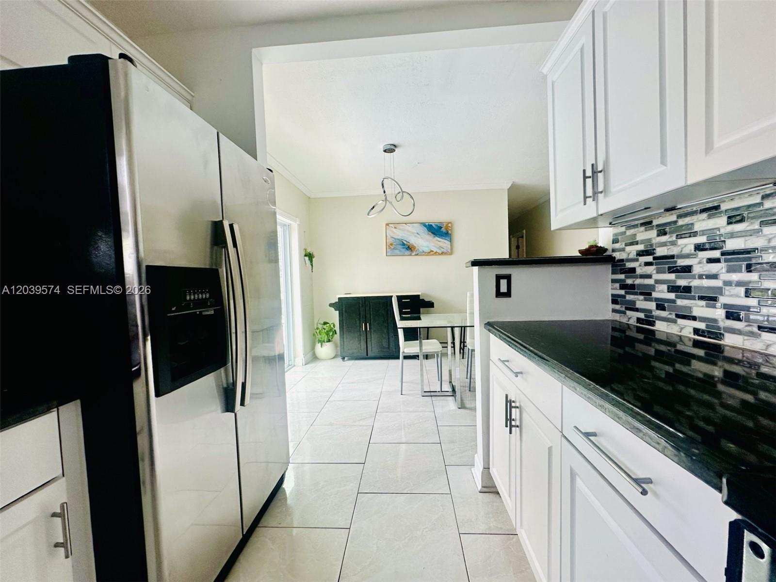 A kitchen with white cabinets, black countertops, and a stainless steel refrigerator faces a dining area — 7021 Scott St., Hollywood FL 33024, HOLLYWOOD, FL