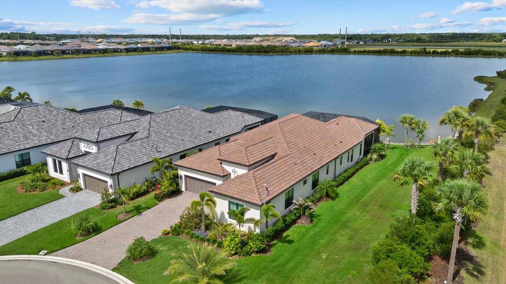 An aerial view shows two single-story houses with tiled roofs situated beside a large lake — 556 BOCELLI DRIVE, NOKOMIS, FL