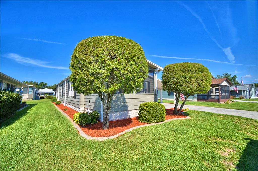 A light-colored mobile home features a manicured lawn, trimmed trees, and red mulch landscaping — 4901 COLONNADES CIRCLE E, LAKELAND, FL