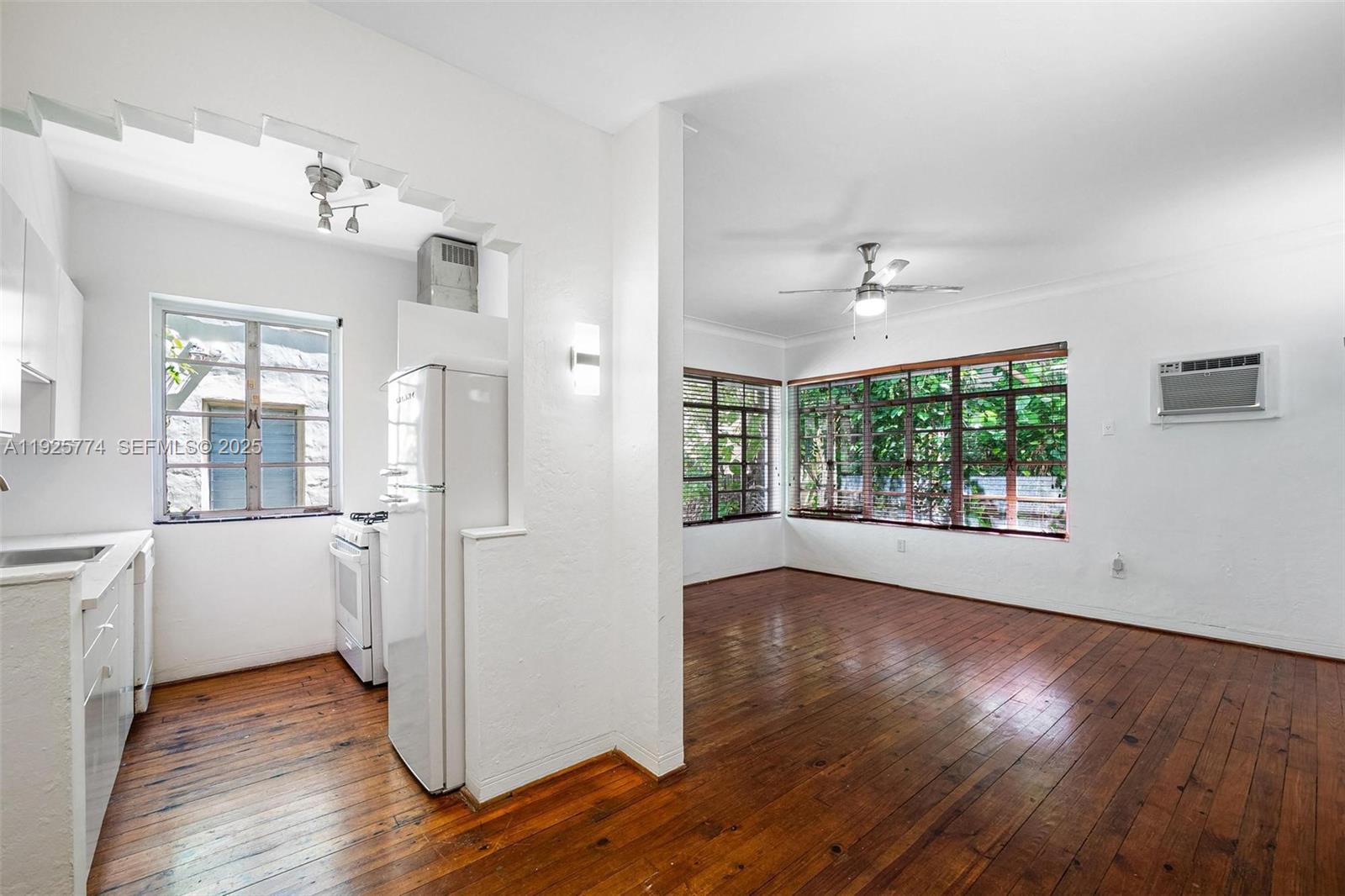 A kitchen with white appliances opens into a living area with hardwood floors and windows — 1611 Euclid Ave # 8, Miami Beach FL 33139, MIAMI BEACH, FL