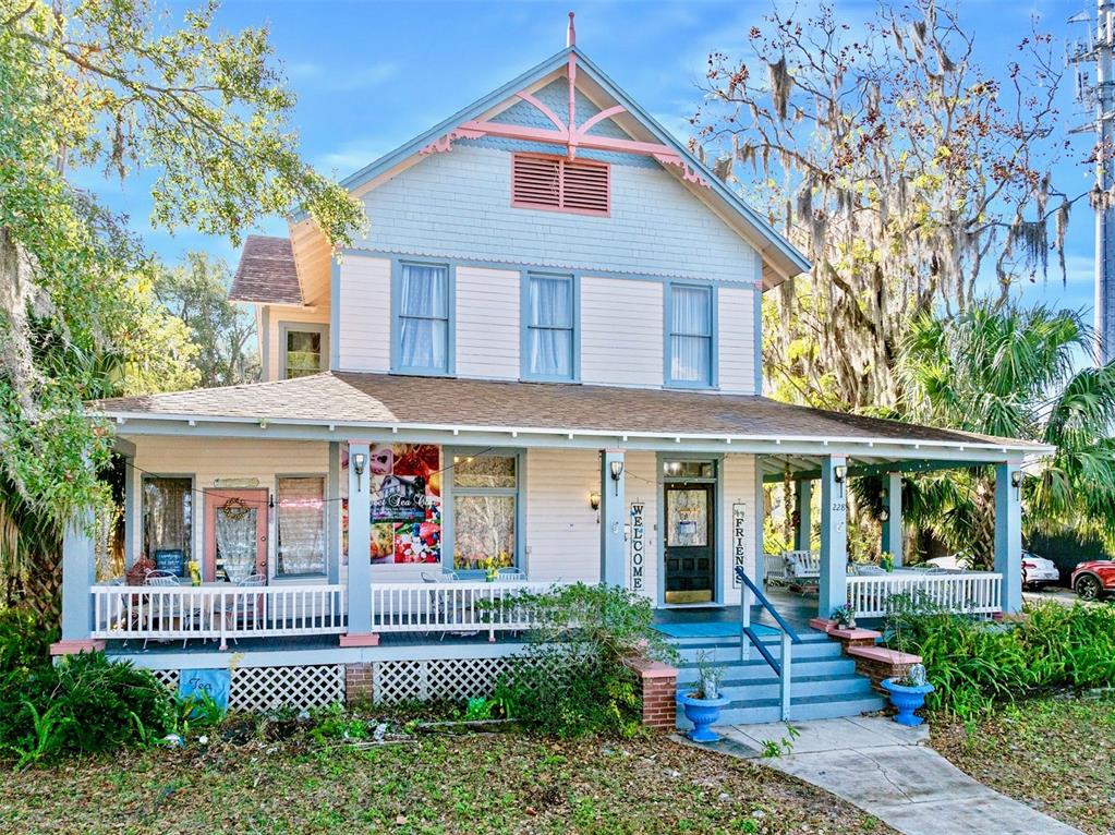 A two-story house with a large front porch, light-colored siding, and blue trim — 228 W HOWRY AVENUE, DELAND, FL