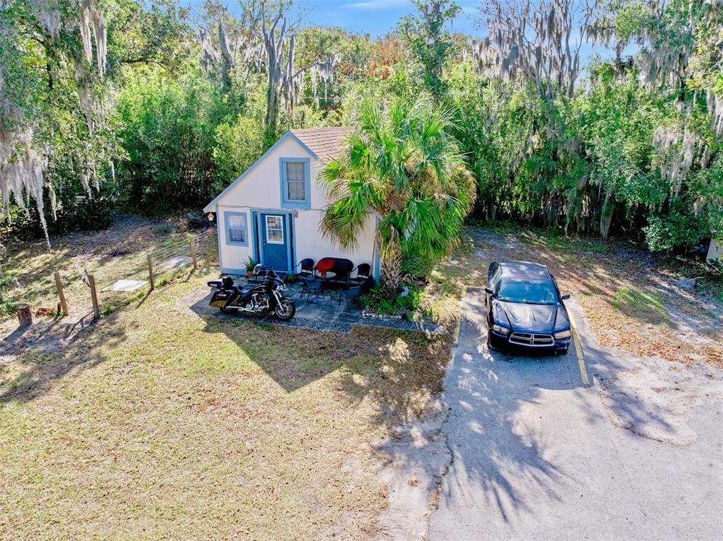 A small, light-colored cottage with a blue door sits next to a parked car and motorcycle — 228 W HOWRY AVENUE, DELAND, FL