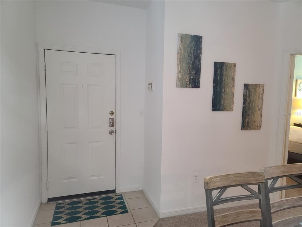 An entryway features a white door, tiled floor, and three abstract paintings on the wall — 8908 LEGACY COURT UNIT 104, KISSIMMEE, FL