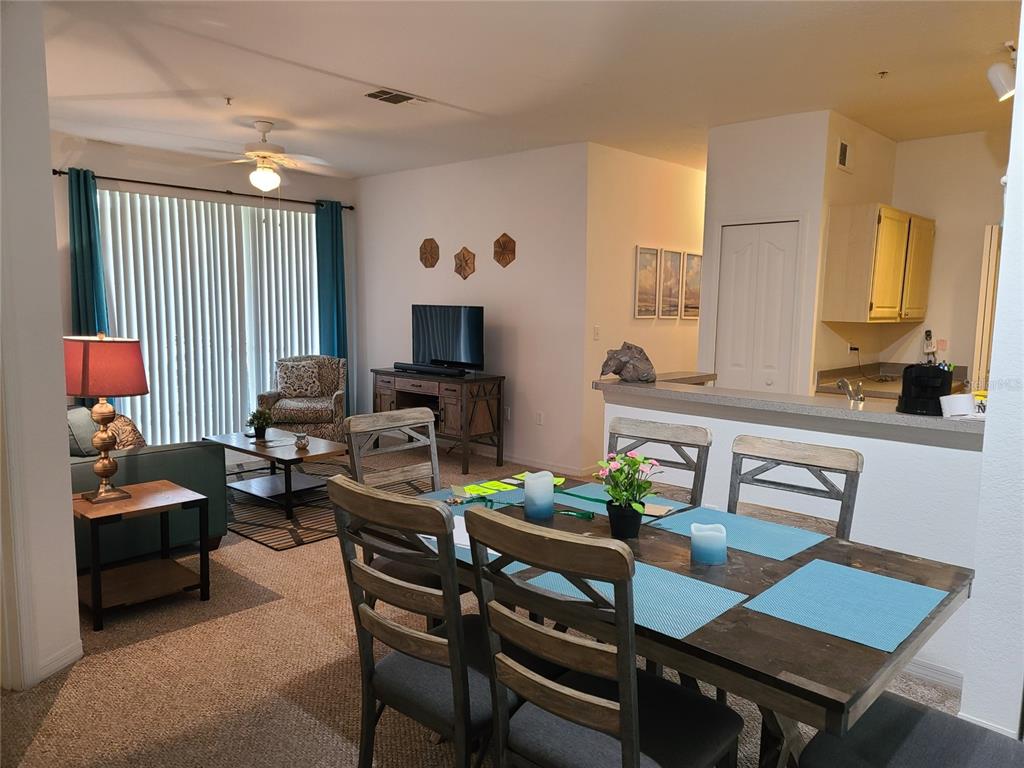 An open-concept living and dining area features a wooden table, sofa, and kitchen pass-through — 8908 LEGACY COURT UNIT 104, KISSIMMEE, FL