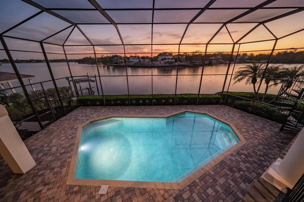 A screened-in pool patio overlooks a waterfront view at sunset with paved decking — 62 CENTRAL COURT, TARPON SPRINGS, FL