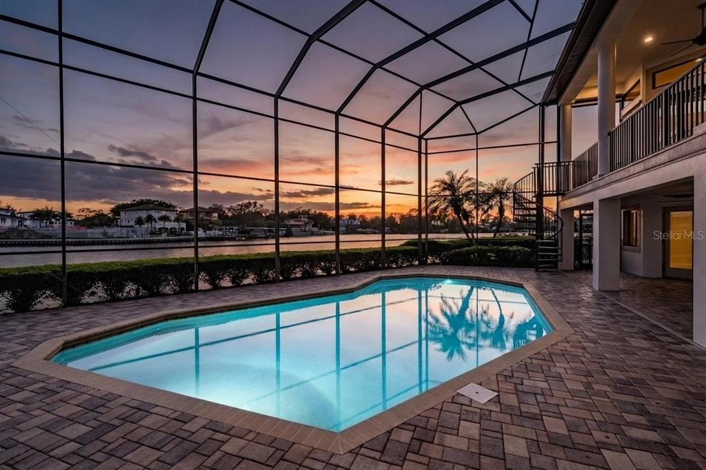 A screened-in swimming pool patio overlooks a canal at sunset with a spiral staircase nearby — 62 CENTRAL COURT, TARPON SPRINGS, FL
