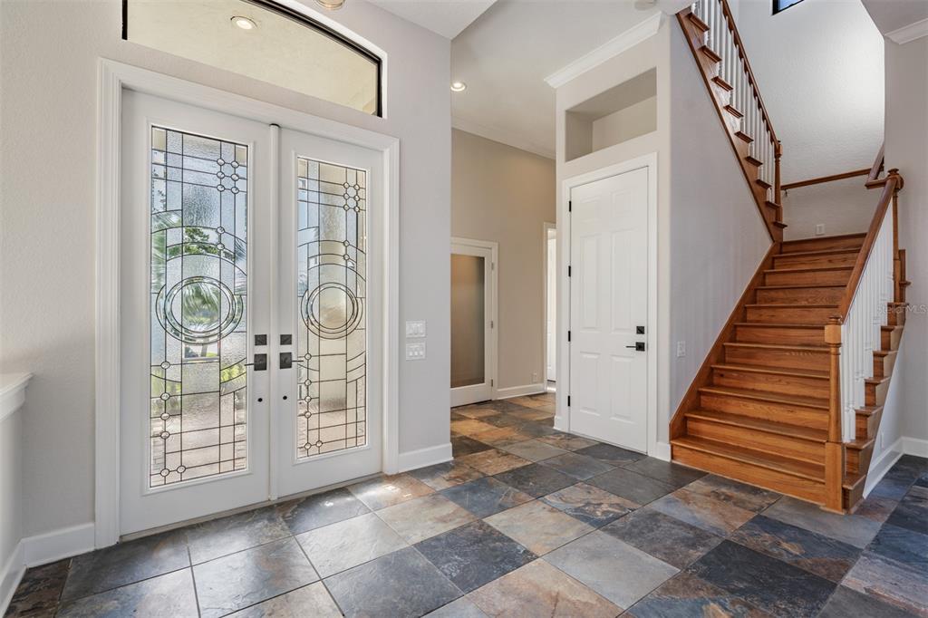 An entryway features a slate tile floor, double glass-paneled doors, and a wooden staircase — 62 CENTRAL COURT, TARPON SPRINGS, FL
