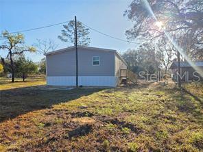 The exterior of a light-colored manufactured home sits on a grassy lot with trees — 12070 NE 63RD PLACE, WILLISTON, FL