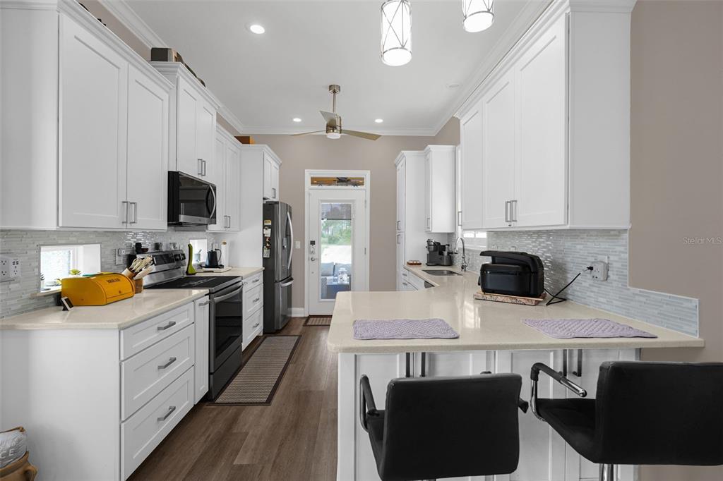 A modern kitchen features white cabinetry, quartz countertops, stainless steel appliances, and a breakfast bar — 3261 FISH HAWK DRIVE, POLK CITY, FL