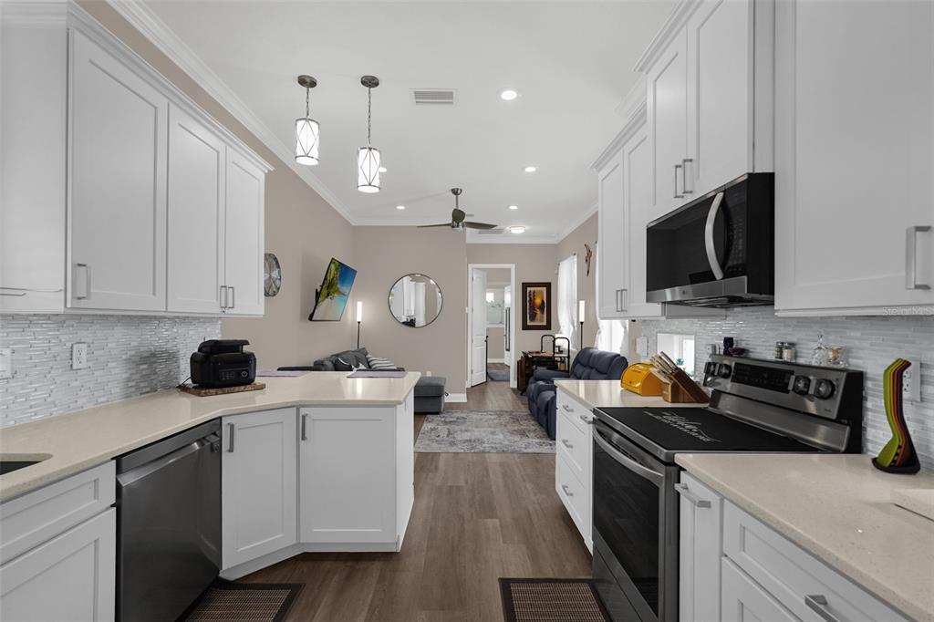 A white kitchen with quartz countertops and stainless steel appliances opens into a living area — 3261 FISH HAWK DRIVE, POLK CITY, FL