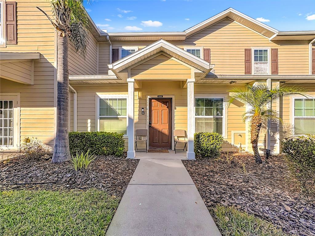 A tan two-story townhouse exterior features a covered entryway, brown front door, and palm trees — 8986 SHINE DRIVE, KISSIMMEE, FL