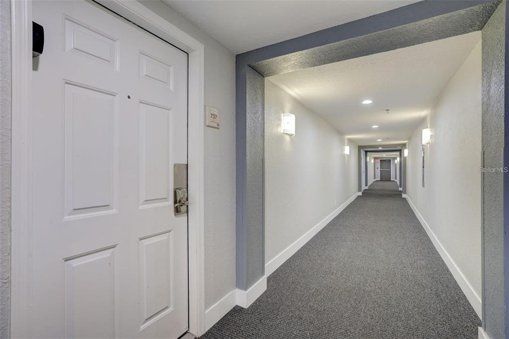 A white apartment door with a number plate opens into a long, carpeted residential hallway — 3100 PARKWAY BOULEVARD UNIT 737, KISSIMMEE, FL
