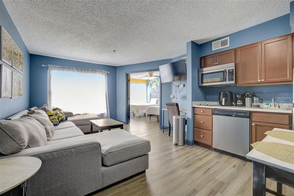 A living room with a gray sectional sofa opens into a bedroom and small kitchen — 3100 PARKWAY BOULEVARD UNIT 737, KISSIMMEE, FL