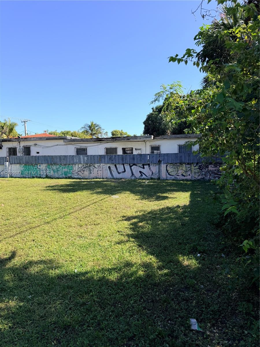 A grassy vacant lot is enclosed by a graffiti-covered wooden fence in front of a building — 5455 NE 3rd Ave, Miami FL 33137, MIAMI, FL