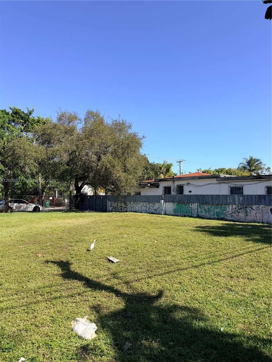 A vacant, grassy lot is enclosed by a graffiti-covered fence with trees in the background — 5455 NE 3rd Ave, Miami FL 33137, MIAMI, FL