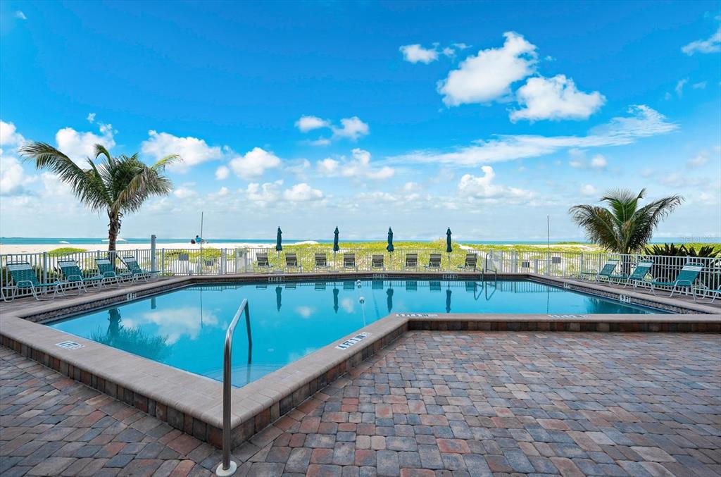A rectangular swimming pool with a brick paver deck overlooks a beach and the ocean — 255 THE ESPLANADE N UNIT 701, VENICE, FL