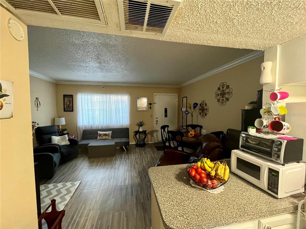 A living room with wood-look flooring, a gray sofa, and a kitchen counter in foreground — 123 BLUE POINT WAY UNIT 110, ALTAMONTE SPRINGS, FL