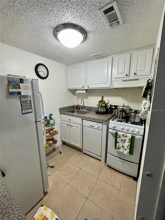 A small kitchen features white cabinets, a white stove, a dishwasher, and tiled flooring — 123 BLUE POINT WAY UNIT 110, ALTAMONTE SPRINGS, FL