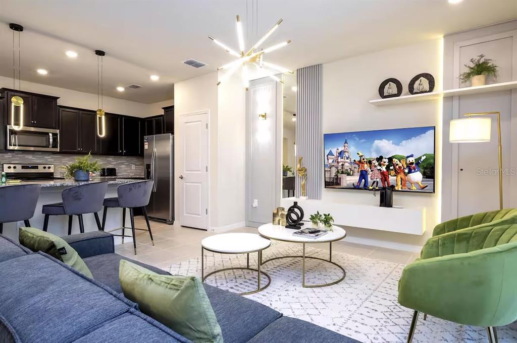 A modern living room features a blue sofa, green armchairs, a television, and an open kitchen — 4294 LANA AVENUE, DAVENPORT, FL