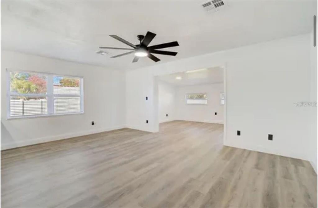 An empty living room with white walls, light wood-look flooring, and a black ceiling fan — 5205 CHENAULT AVENUE, ORLANDO, FL