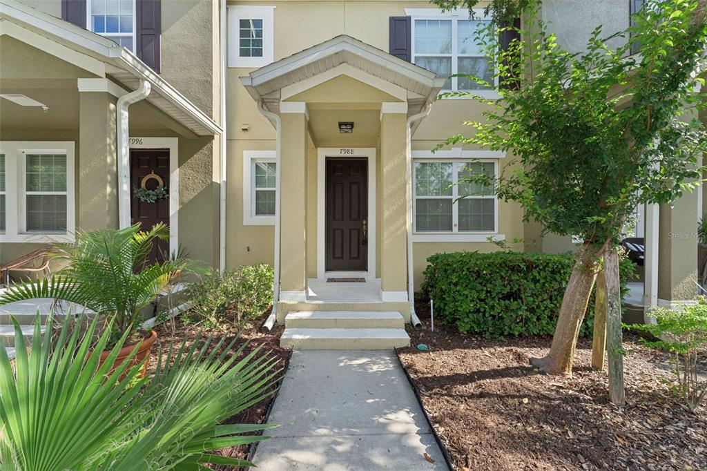 A tan townhouse exterior features a covered entryway with a dark brown front door — 7988 EDGEWOOD FOREST DRIVE, ORLANDO, FL