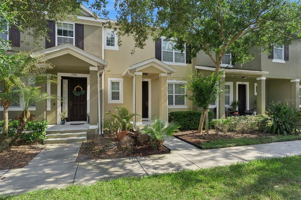 A row of three two-story townhouses with tan stucco facades and covered front porches — 7988 EDGEWOOD FOREST DRIVE, ORLANDO, FL