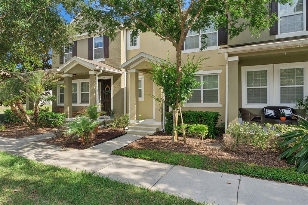 A two-story townhouse exterior with tan siding, a covered entryway, and a front sidewalk — 7988 EDGEWOOD FOREST DRIVE, ORLANDO, FL