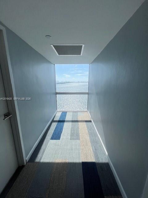 A narrow hallway with blue-toned carpet leads to a large window overlooking the ocean — 3301 NE 5th Ave # 1112, Miami FL 33137, MIAMI, FL