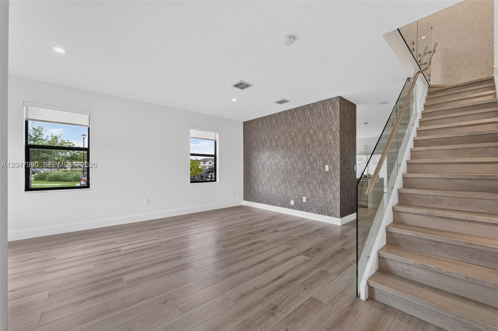An empty living room features wood-look flooring, a patterned accent wall, and a staircase — 10908 W 32nd Ln, Hialeah FL 33018, HIALEAH, FL