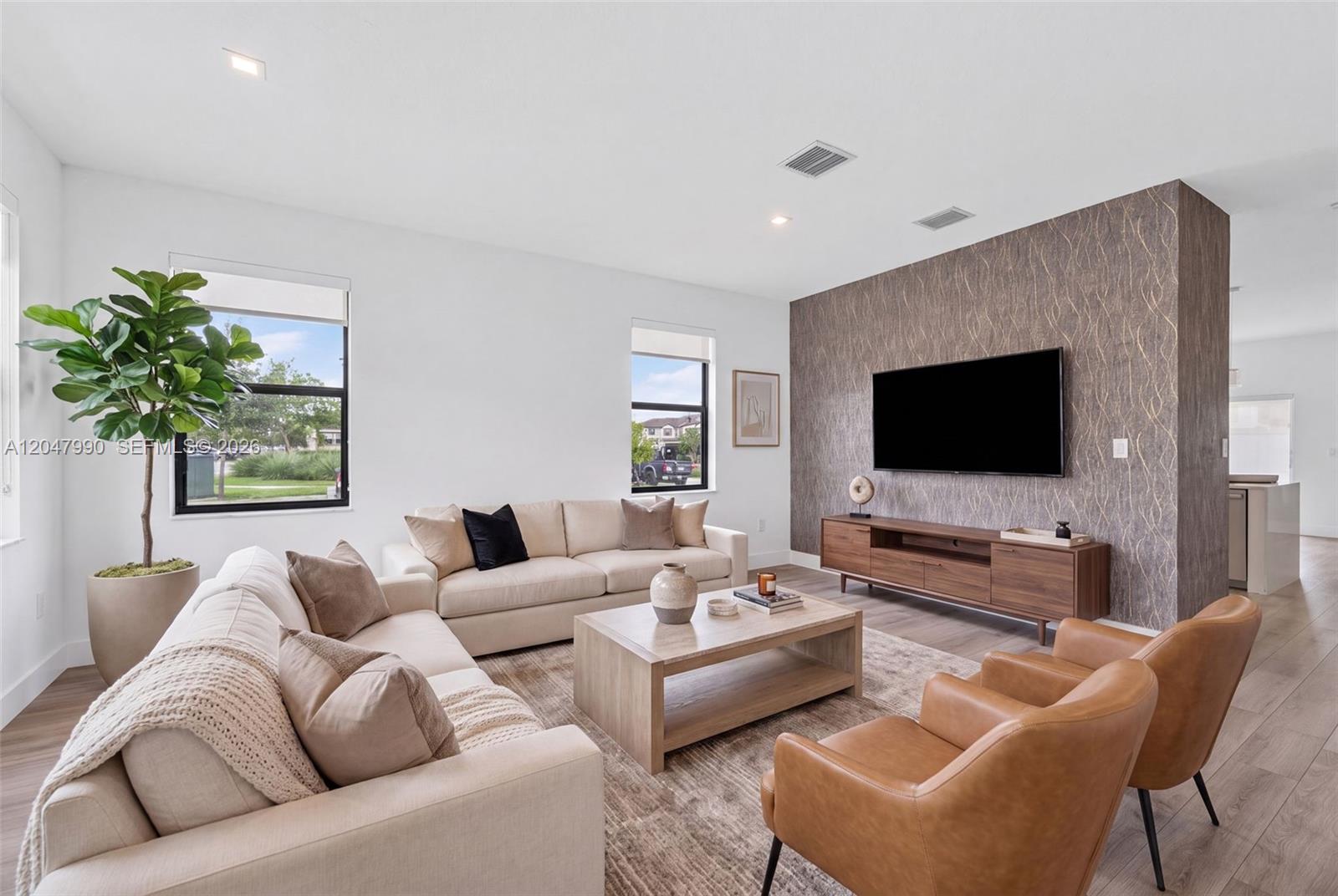 A living room features a textured accent wall, a television, and neutral-toned furniture — 10908 W 32nd Ln, Hialeah FL 33018, HIALEAH, FL