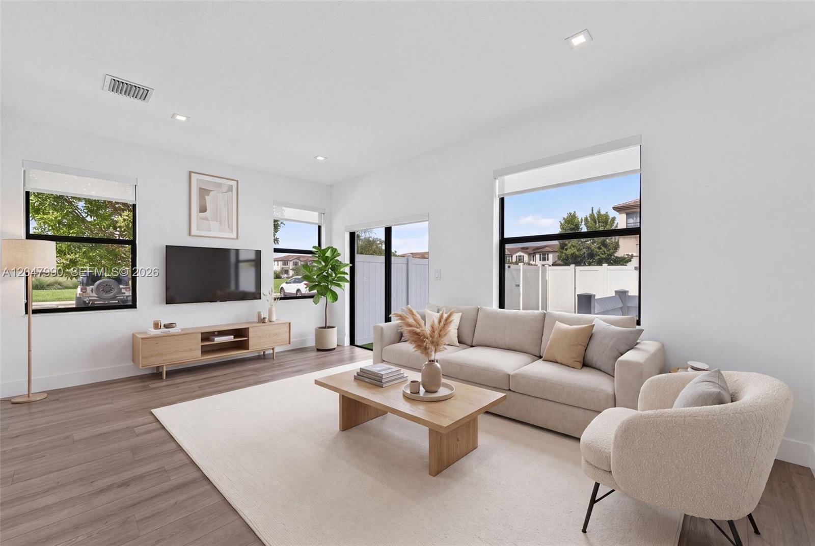 A bright living room features a beige sofa, wooden coffee table, and large windows — 10908 W 32nd Ln, Hialeah FL 33018, HIALEAH, FL