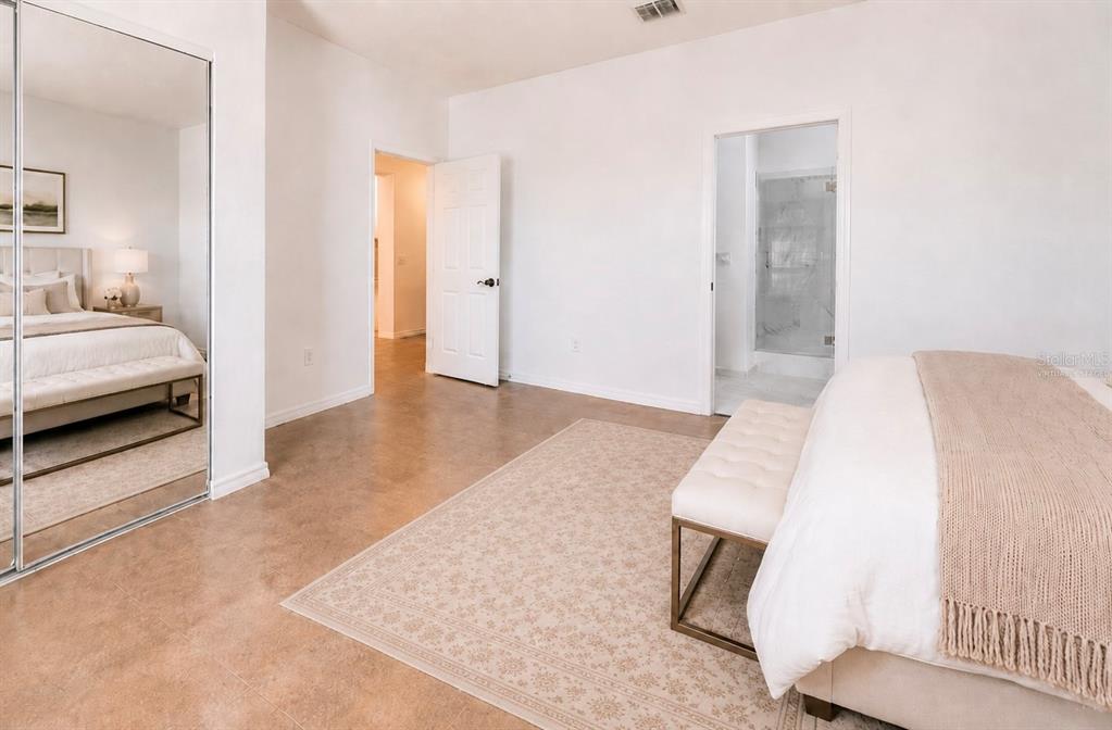 A bedroom with tile flooring, a mirrored closet, a bed with a bench, and an ensuite — 8531 GEDDES LOOP, ORLANDO, FL