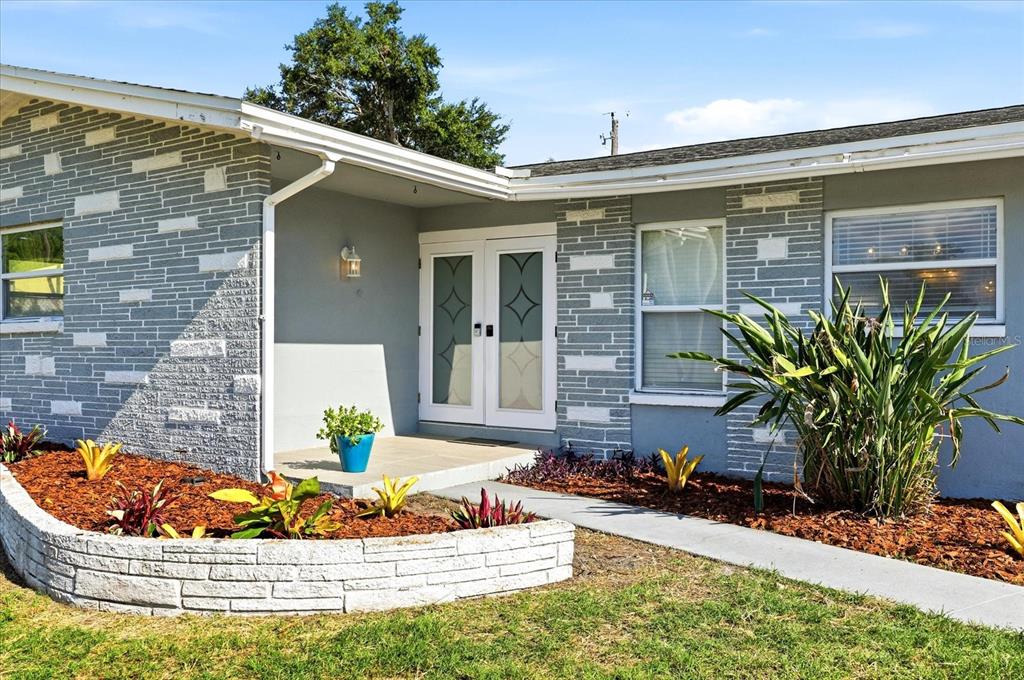 A gray house exterior features a stone facade, double front doors, and a landscaped yard — 1354 62ND AVENUE S, ST PETERSBURG, FL