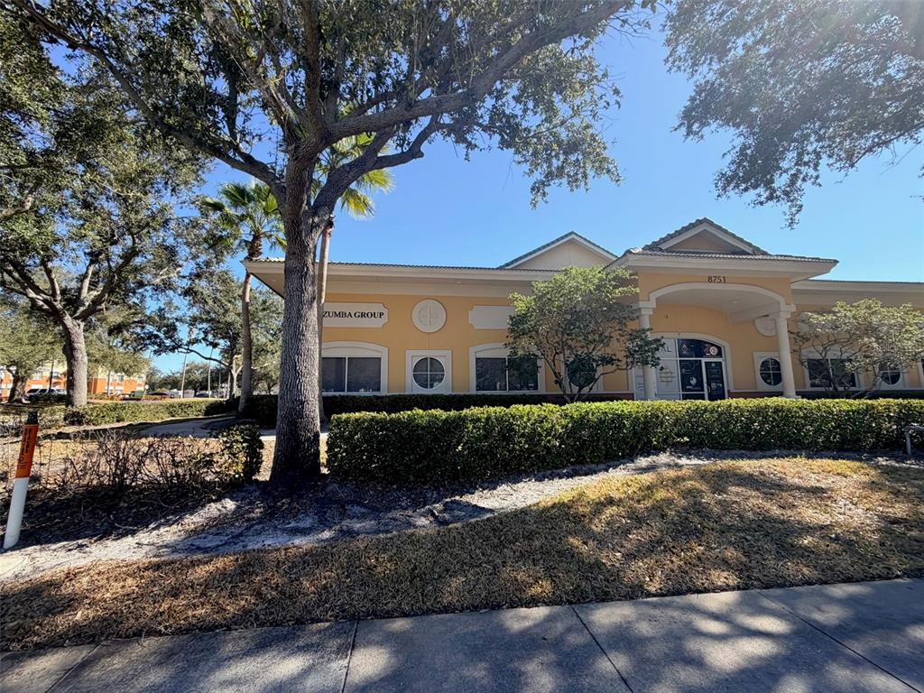 A single-story commercial building with yellow stucco walls and a hedge-lined front lawn — 8751 COMMODITY CIRCLE UNIT 5, ORLANDO, FL