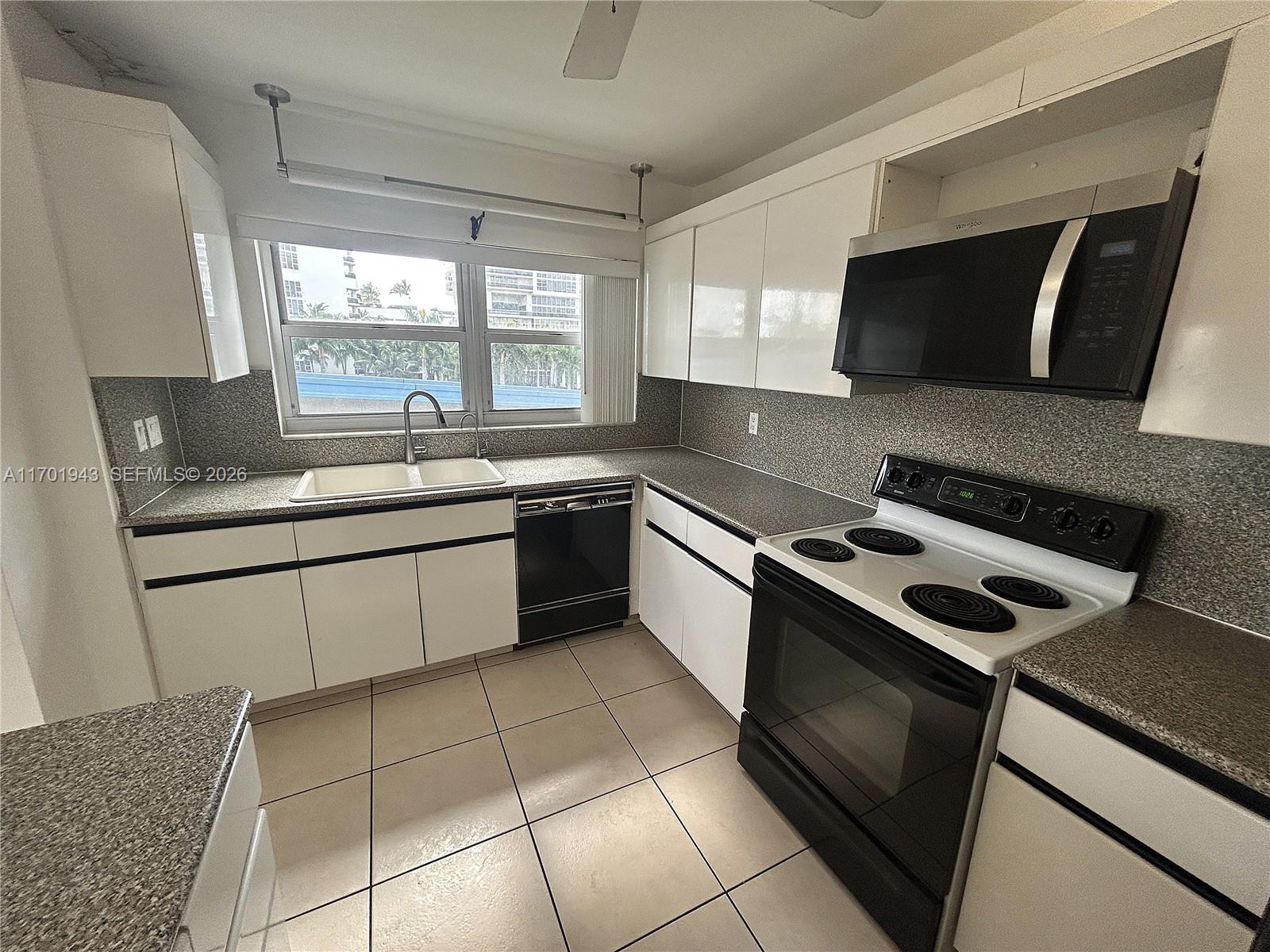 A kitchen features white cabinets, black appliances, speckled countertops, and a large window — 1825 S Ocean Dr # 401, Hallandale Beach FL 33009, HALLANDALE BEACH, FL