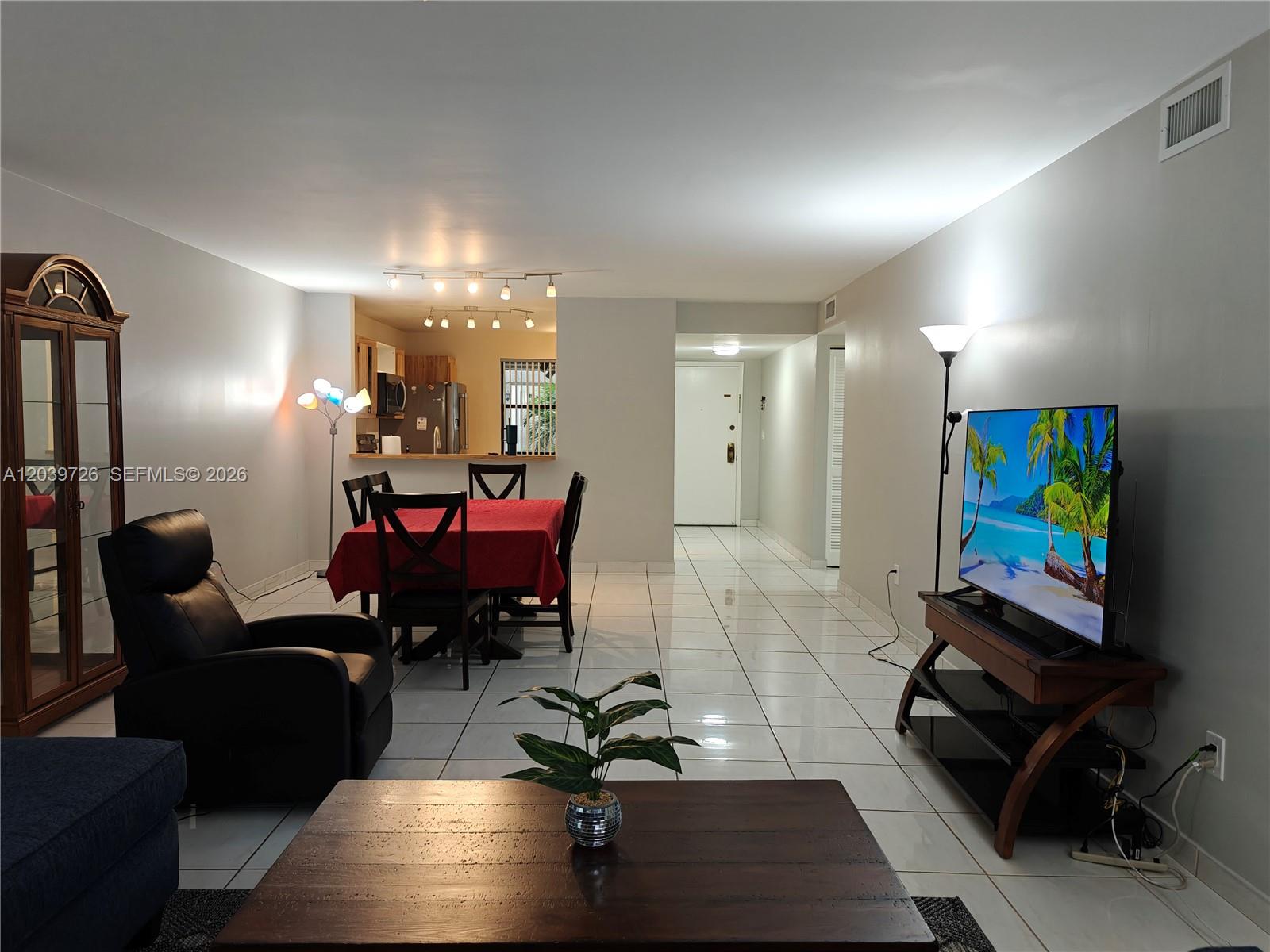 A living and dining area features white tile floors, a red tablecloth, and a television — 601 Ives Dairy Rd # 8, Miami FL 33179, MIAMI, FL