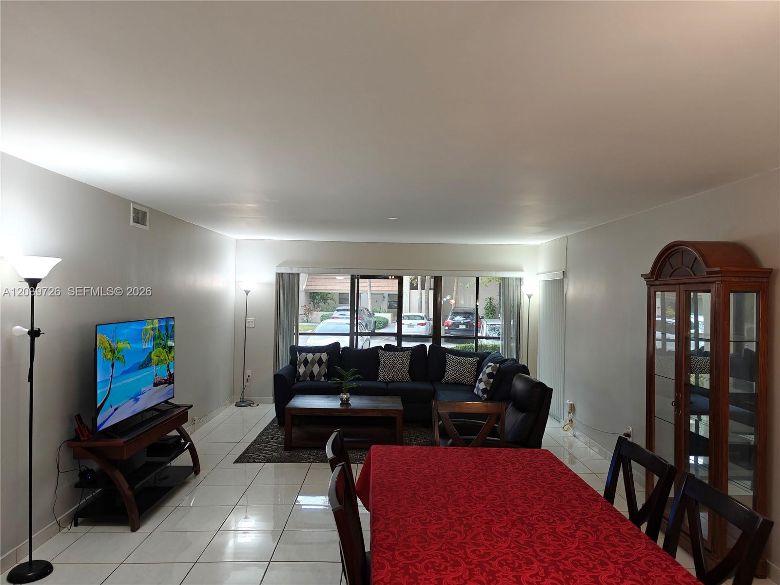 A living and dining area features white tile floors, a sectional sofa, and a television — 601 Ives Dairy Rd # 8, Miami FL 33179, MIAMI, FL