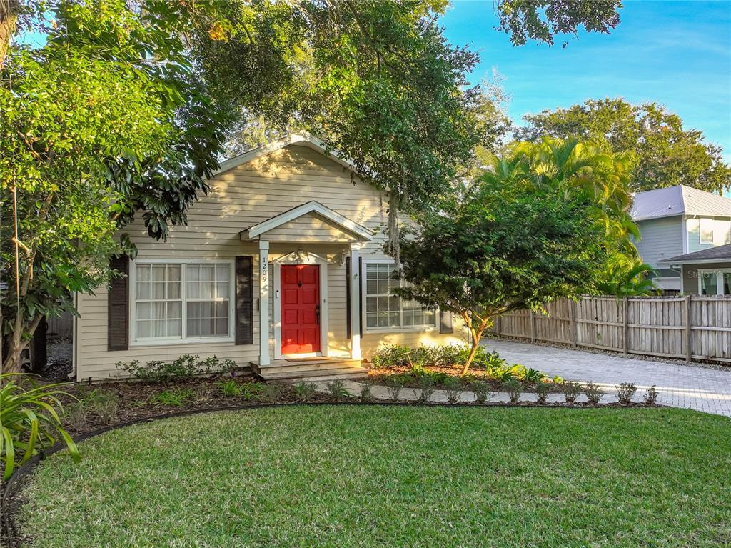 A single-story house with light siding, a red front door, and a landscaped front yard — 1209 CLOUSER AVENUE, ORLANDO, FL