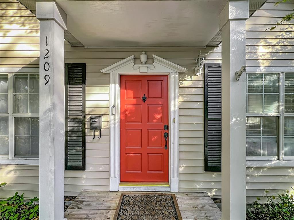 A red front door with a black knocker is centered between two white porch columns — 1209 CLOUSER AVENUE, ORLANDO, FL