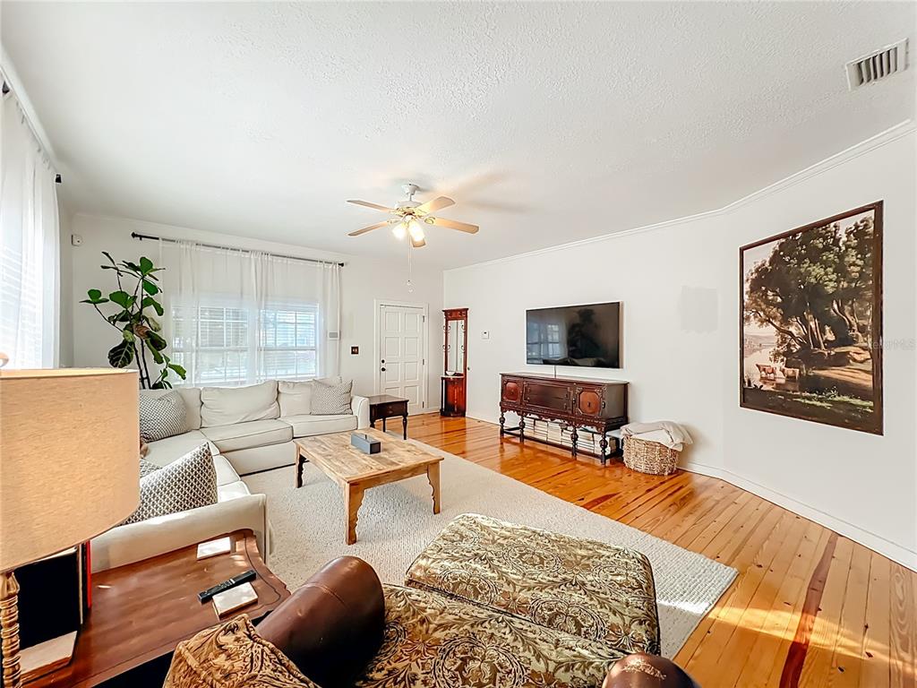 A living room features hardwood floors, a white sectional sofa, a television, and wall art — 1209 CLOUSER AVENUE, ORLANDO, FL