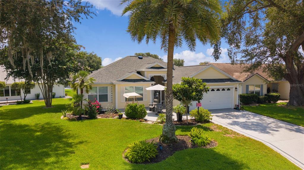 A yellow single-story house with a palm tree, a two-car garage, and a front patio — 9340 SE 170TH HUMPHREYS LOOP, THE VILLAGES, FL