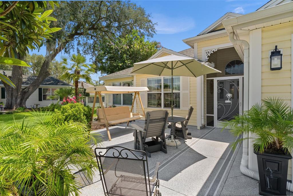 A patio with a swing, table, chairs, and umbrella sits outside a yellow house — 9340 SE 170TH HUMPHREYS LOOP, THE VILLAGES, FL