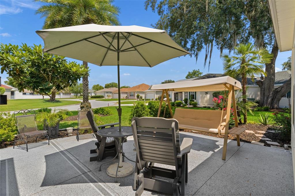 A patio features a table with an umbrella, two chairs, and a covered porch swing — 9340 SE 170TH HUMPHREYS LOOP, THE VILLAGES, FL