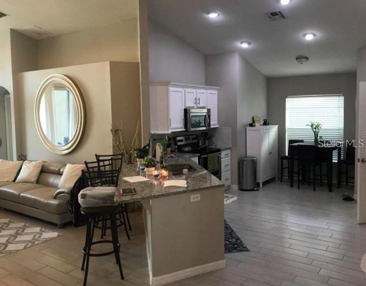An open-concept kitchen with granite countertops and a breakfast bar overlooks a living area — 15142 MASTHEAD LANDING CIRCLE, WINTER GARDEN, FL
