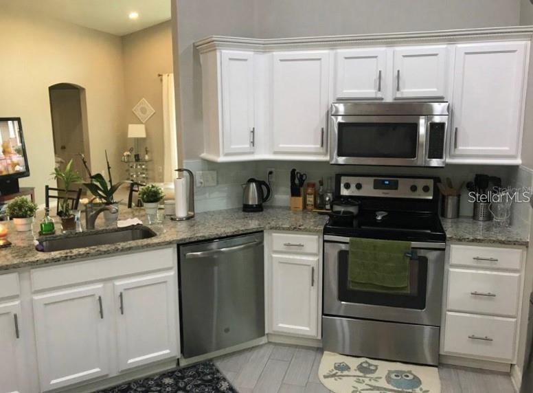 A kitchen features white cabinets, stainless steel appliances, and granite countertops — 15142 MASTHEAD LANDING CIRCLE, WINTER GARDEN, FL