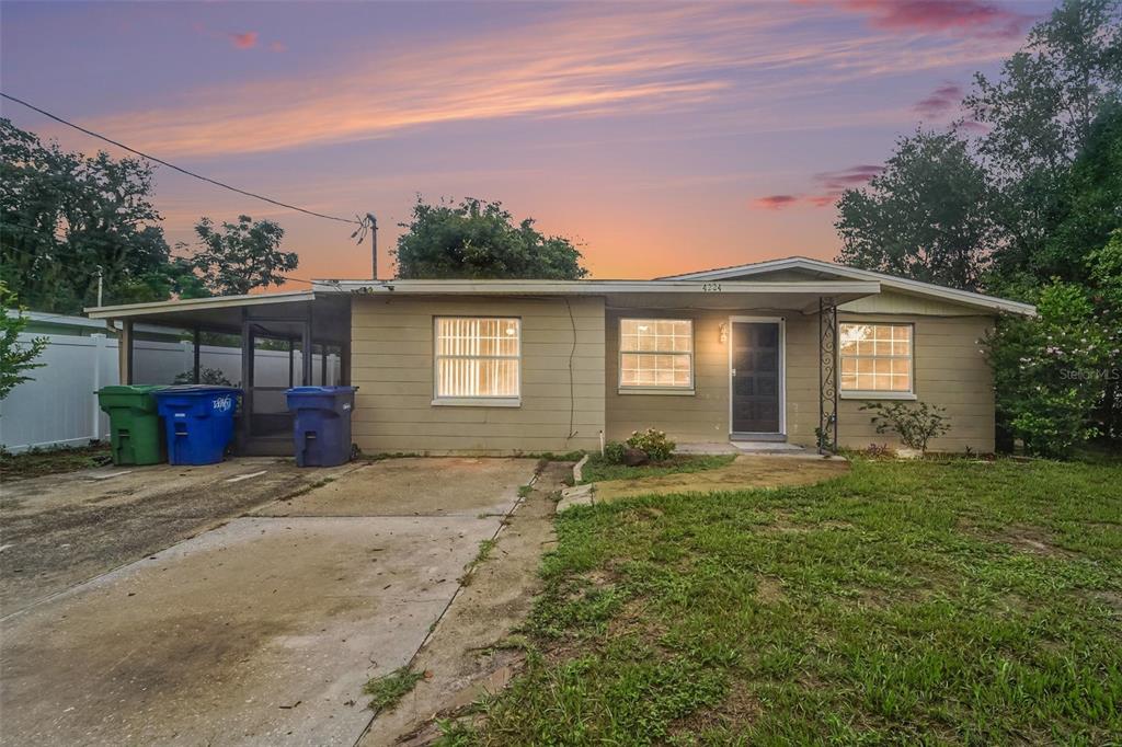 A single-story house with a concrete driveway, a carport, and a front lawn at sunset — 4224 E REGNAS AVENUE, TAMPA, FL