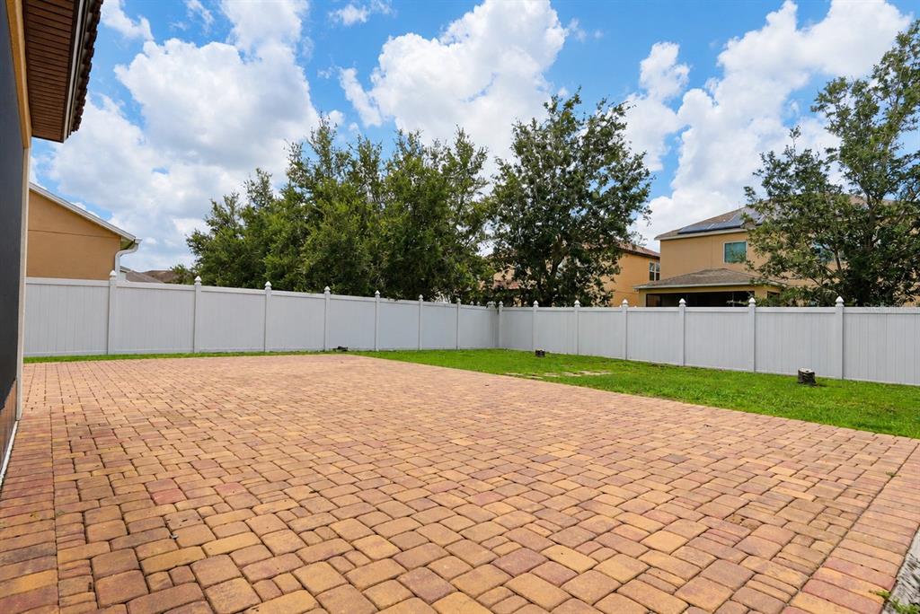 A backyard features a large paved patio area bordered by a white vinyl privacy fence — 9088 OUTLOOK ROCK TRAIL, WINDERMERE, FL