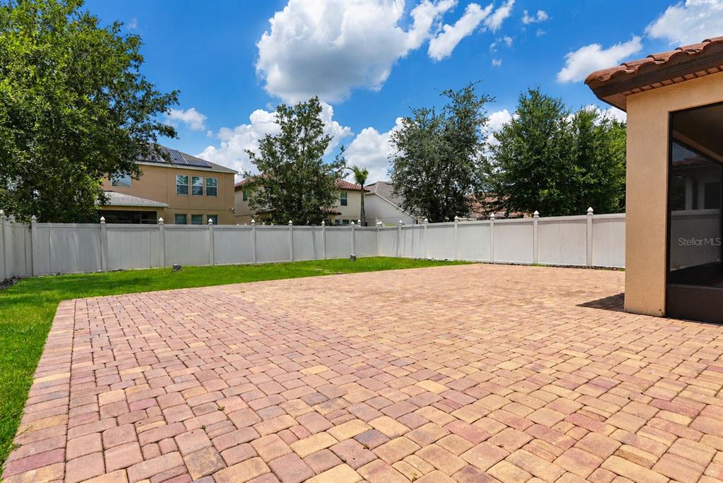 A backyard features a large paver patio, a white vinyl fence, and surrounding residential homes — 9088 OUTLOOK ROCK TRAIL, WINDERMERE, FL