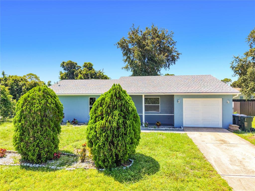 A single-story blue house with a white garage door and two large, rounded evergreen bushes — 4441 MULGRAVE AVENUE, NORTH PORT, FL